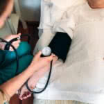 Cuidadora irreconhecível verificando a pressão arterial para uma mulher idosa em casa