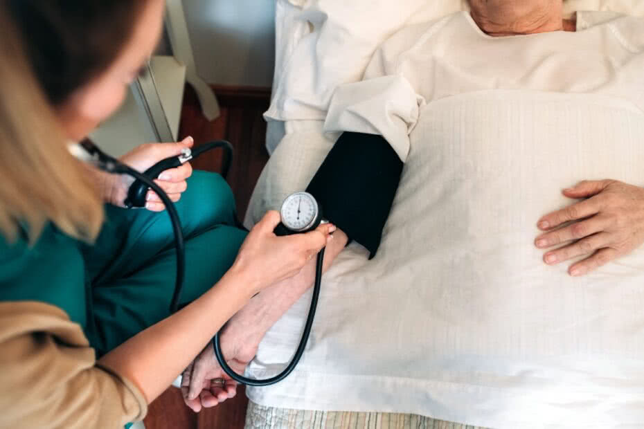 Cuidadora irreconhecível verificando a pressão arterial para uma mulher idosa em casa