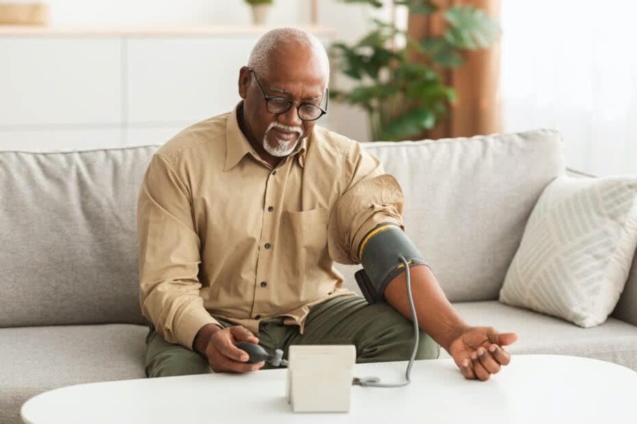 Problema de hipertensão na terceira idade. Homem afro-americano medindo pressão arterial usando esfigmomanômetro manguito sentado no sofá em casa. Cuidados de saúde, problema de saúde